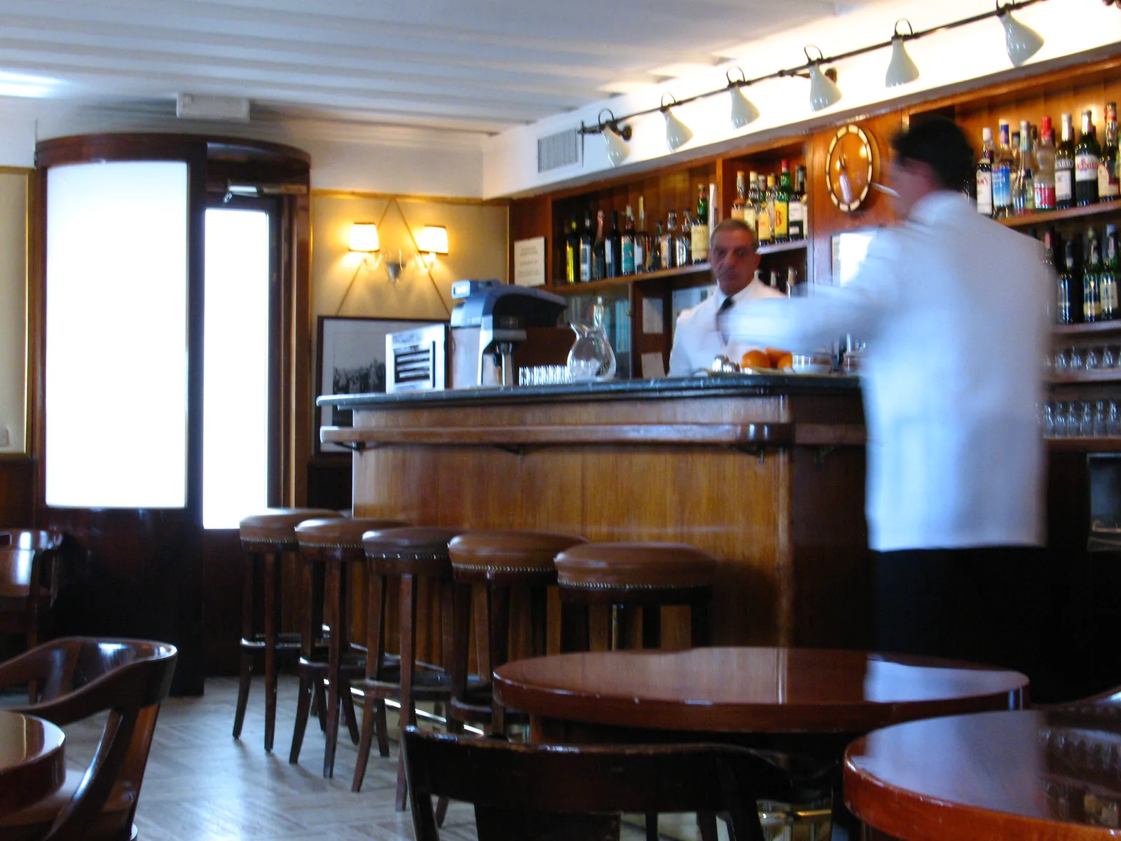 Зал Harry's Bar: круглые столики, табуреты у стойки, бармен за работой